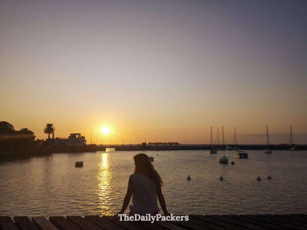 Voyageur assis sur la jetée au coucher du soleil à Colonia del Sacramento, regardant le soleil se coucher derrière le port.