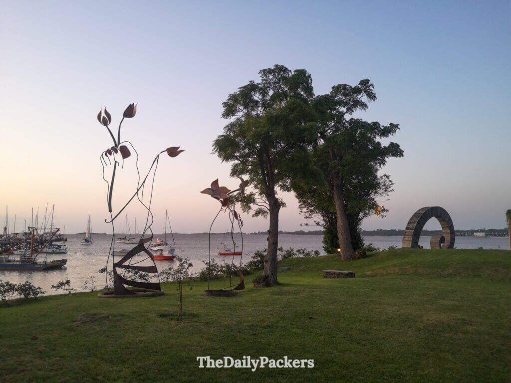 Sculptures métalliques artistiques et arbres au Bastión del Carmen Cultural Center avec des bateaux amarrés le long du Río de la Plata.