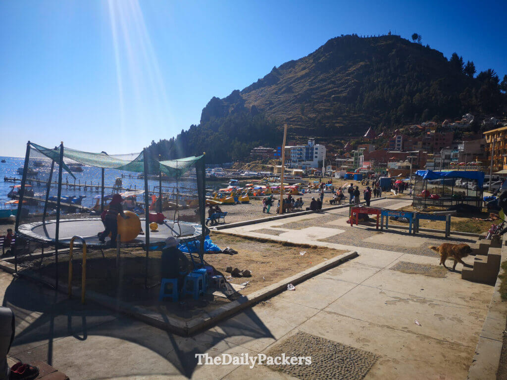 Busy waterfront in Copacabana with pedal boats, families, and mountain scenery in the background