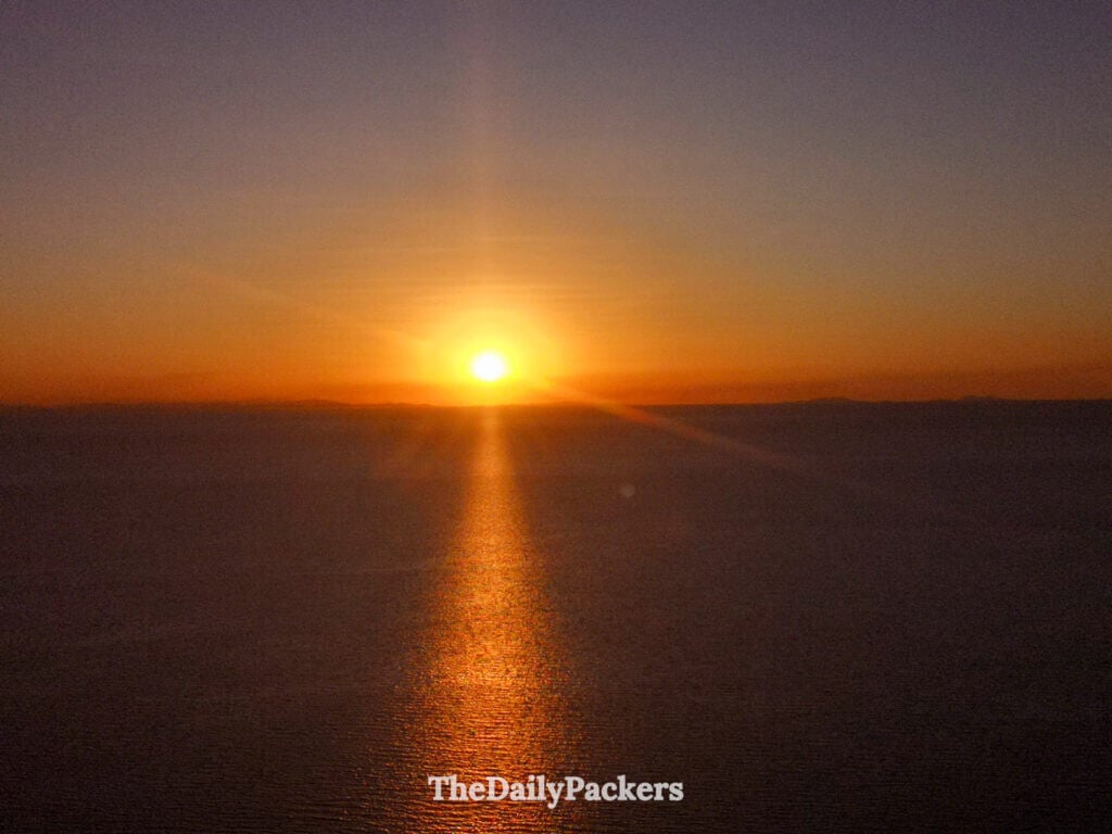 Close-up sunset over Lake Titicaca with deep orange tones and a long shimmering reflection across the still water.