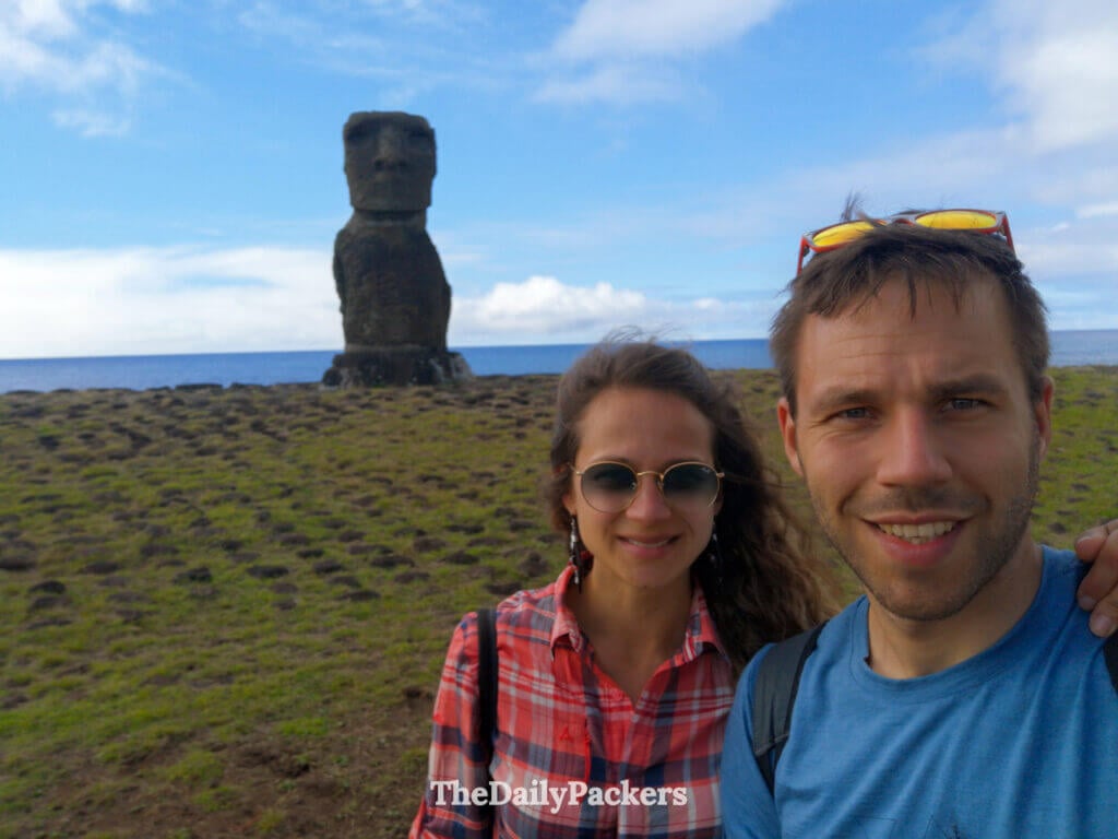 Selfie of two travelers in front of the solitary Moai at Ahu Hanga Kioe, Easter Island, with the Pacific Ocean stretching behind them.