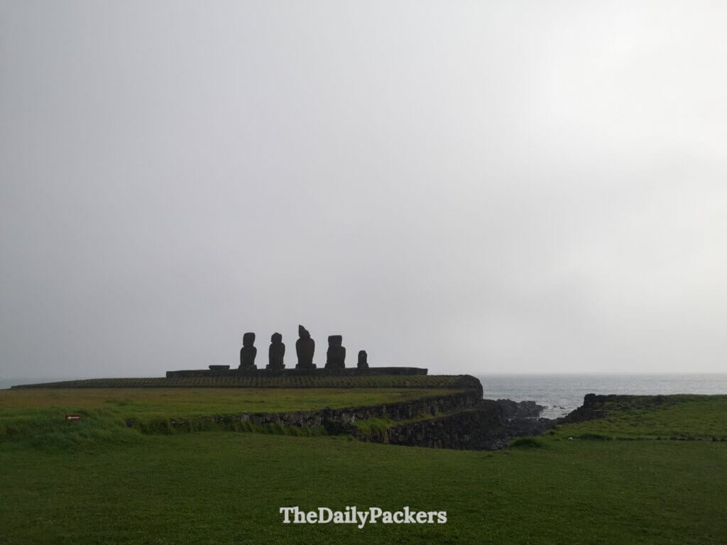 Ahu Vai Ure platform with multiple Moai statues overlooking Hanga Roa’s coastline under dramatic cloudy skies.