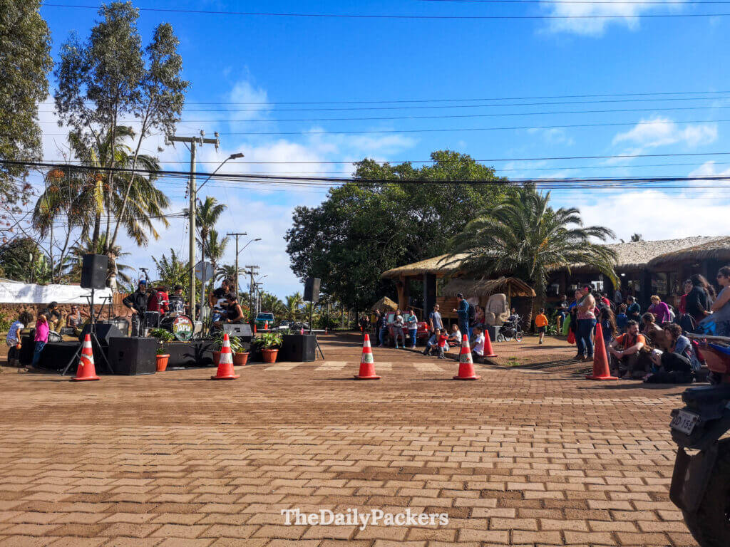Crowd gathered around a live outdoor concert in Hanga Roa, enjoying local music under the palm trees and island sunshine.