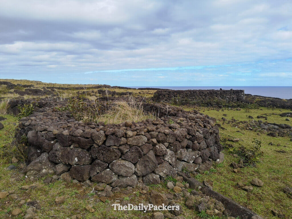 Circular stone foundations of ancient Rapa Nui houses near Ana Te Pora, overlooking the Pacific Ocean and surrounded by volcanic terrain.