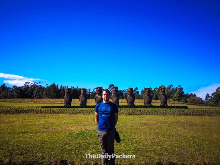 traveler standing in front of ahu akivi’s seven aligned moai statues while hiking the Te Ana coastal trail in the easter island national park during a sunny day