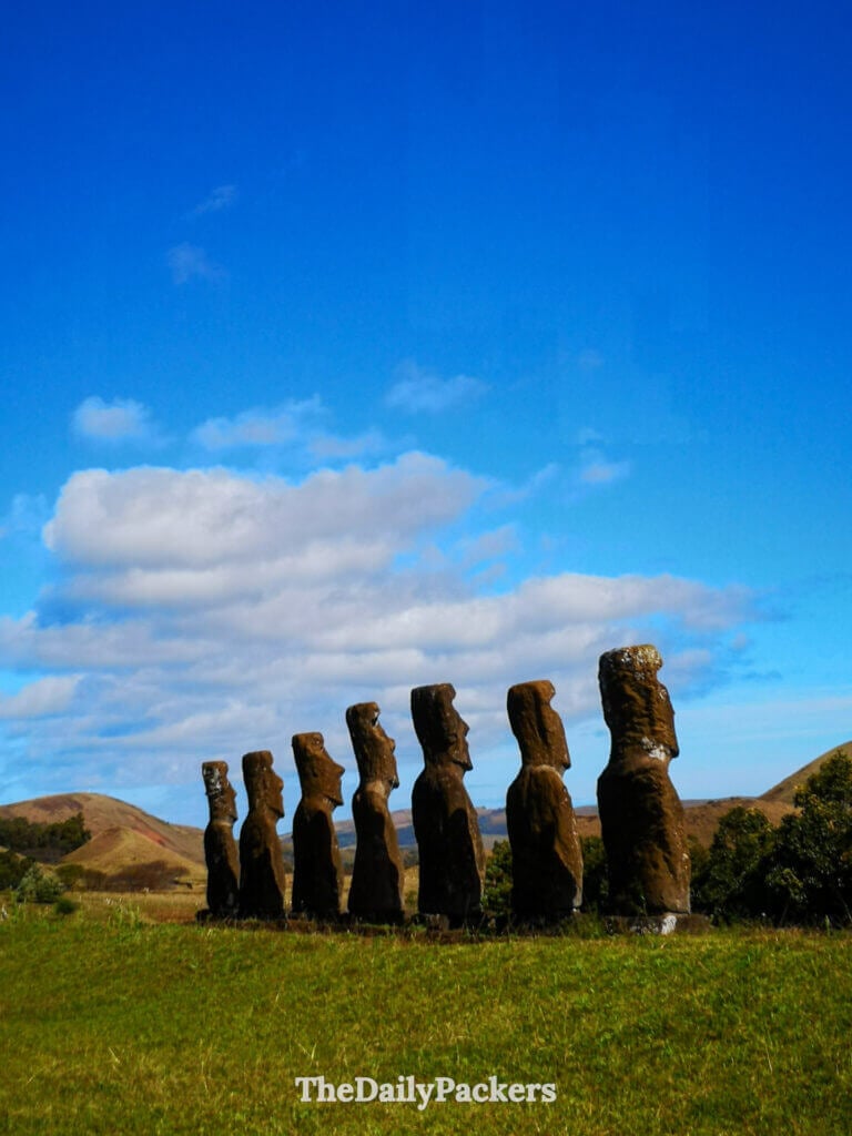standing moai statues at ahu akivi on easter island surrounded by grassy hills under a bright blue sky