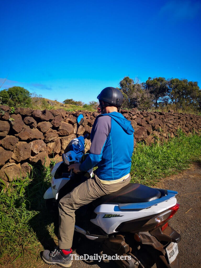 Traveler riding a scooter along a rural stone-walled road on Easter Island, a popular way to explore remote archaeological sites around Rapa Nui.