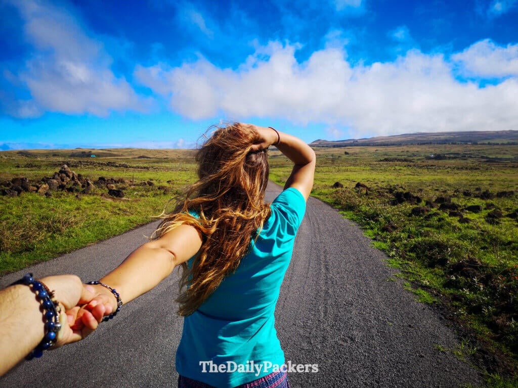 Woman walking ahead on a rural road on Easter Island, surrounded by open volcanic landscapes and dramatic coastal scenery during an Easter island Road Trip