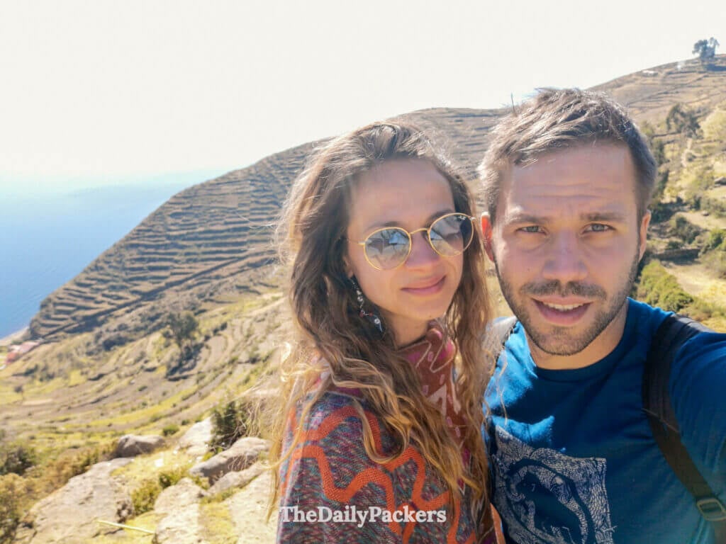 couple selfie on isla del sol with terraced hills and lake Titicaca stretching behind them