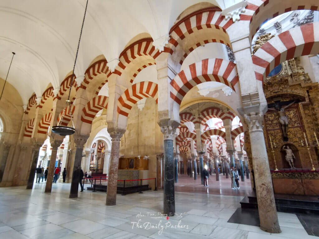 Une large salle de la section originale de la mosquée montrant des rangées d'arches rayées rouge et blanc soutenues par des colonnes de pierre sur un spacieux sol en terre cuite.