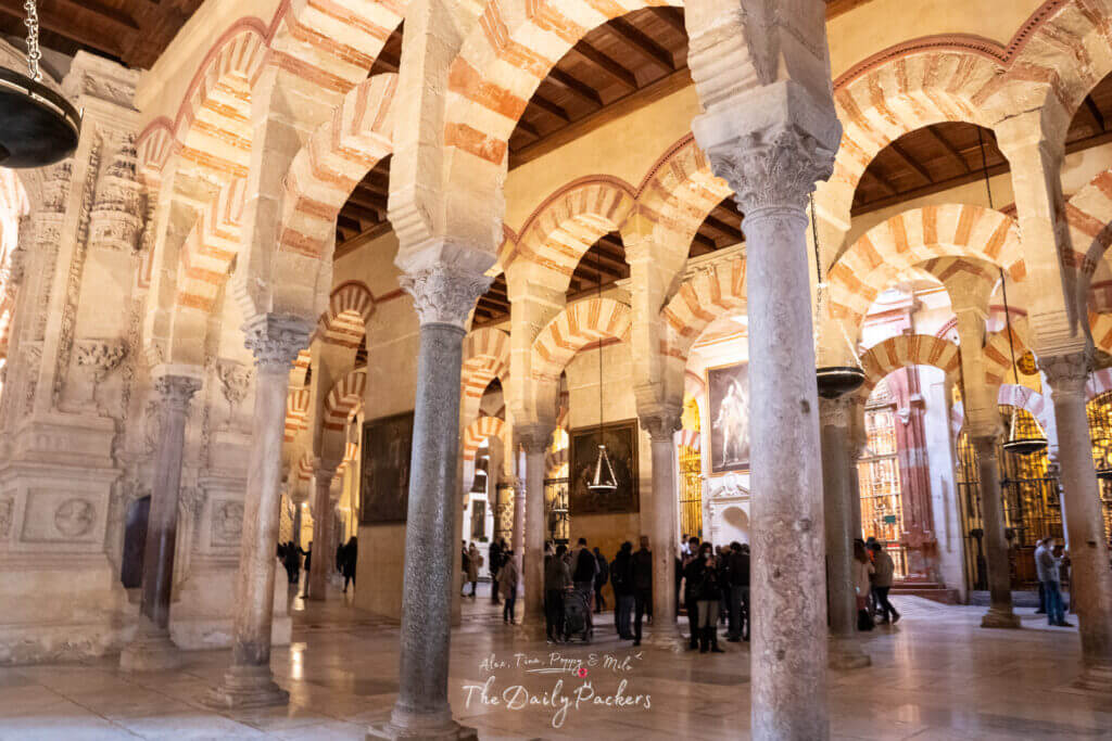 Vue intérieure de la mezquita de Cordoue avec des arches rouges et blanches superposées, des piliers de pierre et des visiteurs explorant la salle de prière historique