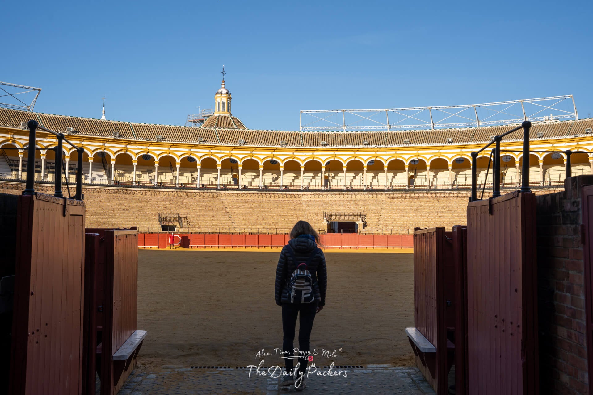 Traveler walking into the iconic bullring of Seville through the arena gates, with sunlight illuminating the stands.