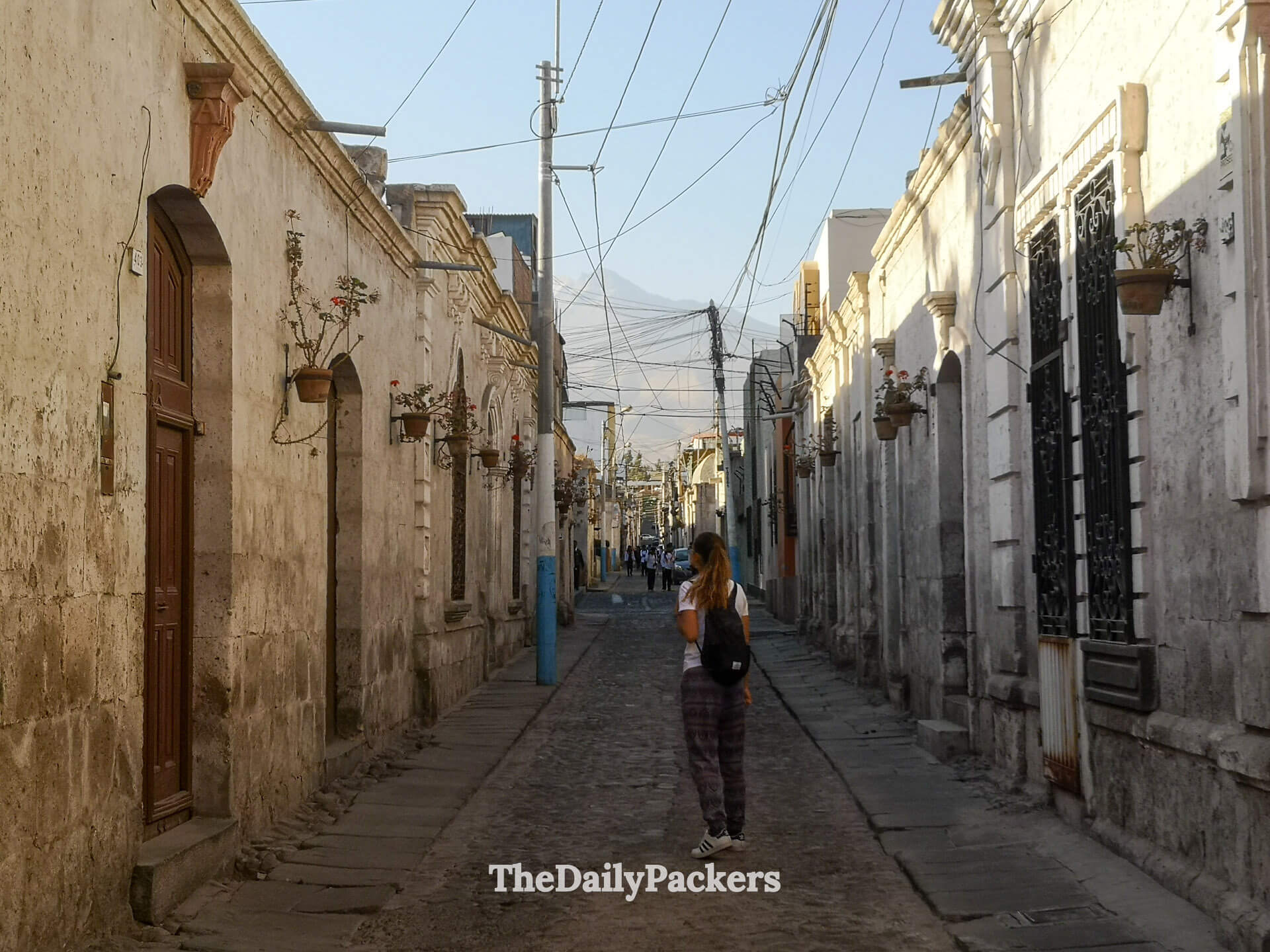 Quiet colonial street in the Yanahuara district of Arequipa with white sillar stone houses, cobblestones, and a local walking toward the viewpoint