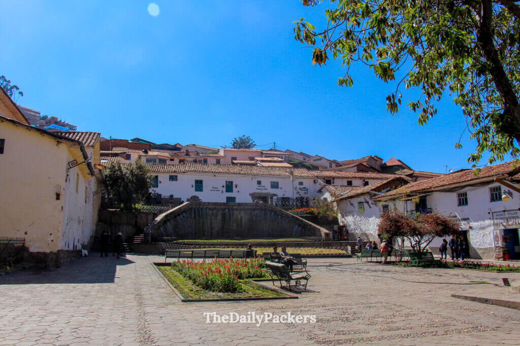 Peaceful San Blas Plaza in Cusco, Peru, with terraced fountain, benches, and white colonial houses overlooking the hillside neighborhood.