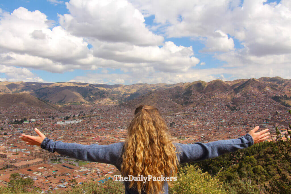 Back view of a visitor overlooking the entire city of Cusco from the Cristo Blanco viewpoint, with sprawling rooftops and Andean mountains.