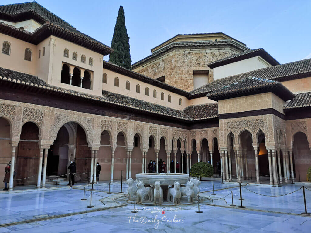 Vue grand angle de la Cour des Lions à l'Alhambra de Grenade, mettant en valeur l'architecture islamique complexe et les arcades symétriques.