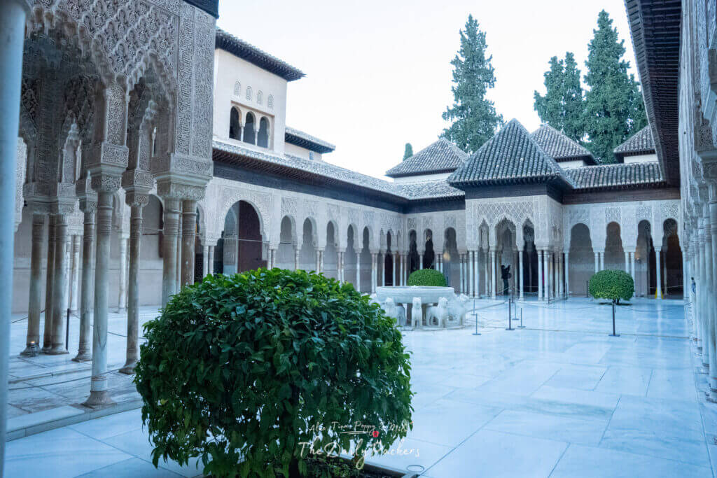 Cour des Lions au Palais de Comares de l'Alhambra, présentant des arches sculptées emblématiques, des colonnes de marbre et la fontaine centrale aux lions entourée d'allées paisibles.