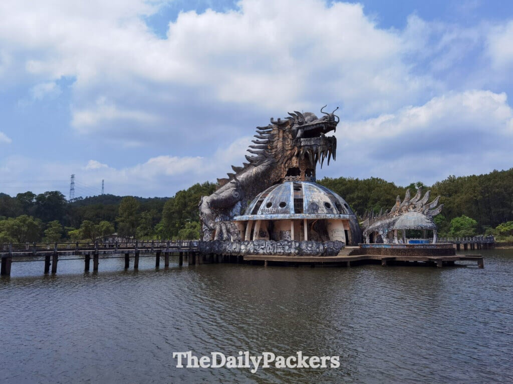 Lake-level perspective of the abandoned dragon aquarium at Thuy Tien Lake, highlighting its imposing sculpted head and the walkways extending across the water