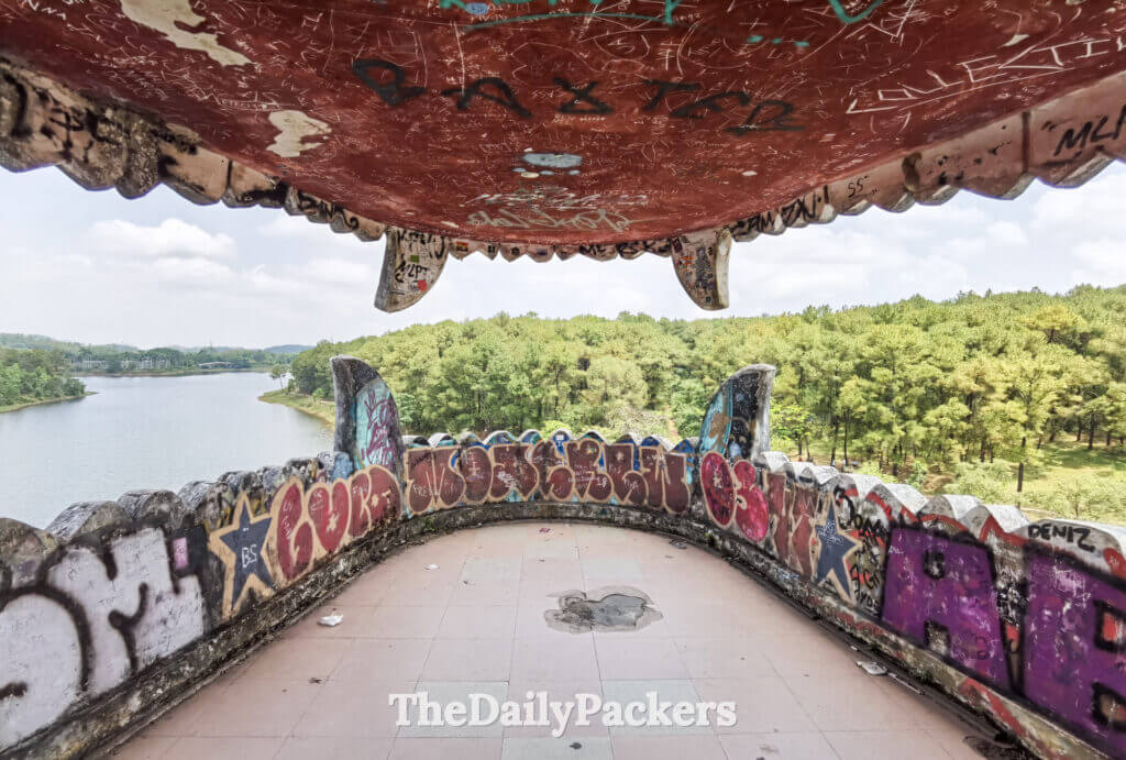 View from inside the dragon’s mouth at Thuy Tien Lake, overlooking the forest and lake through graffiti-covered concrete.