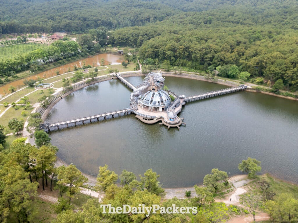Aerial view of the abandoned Thuy Tien Lake waterpark near Hue, Vietnam, showing the dragon structure rising from the lake and surrounded by dense forest.