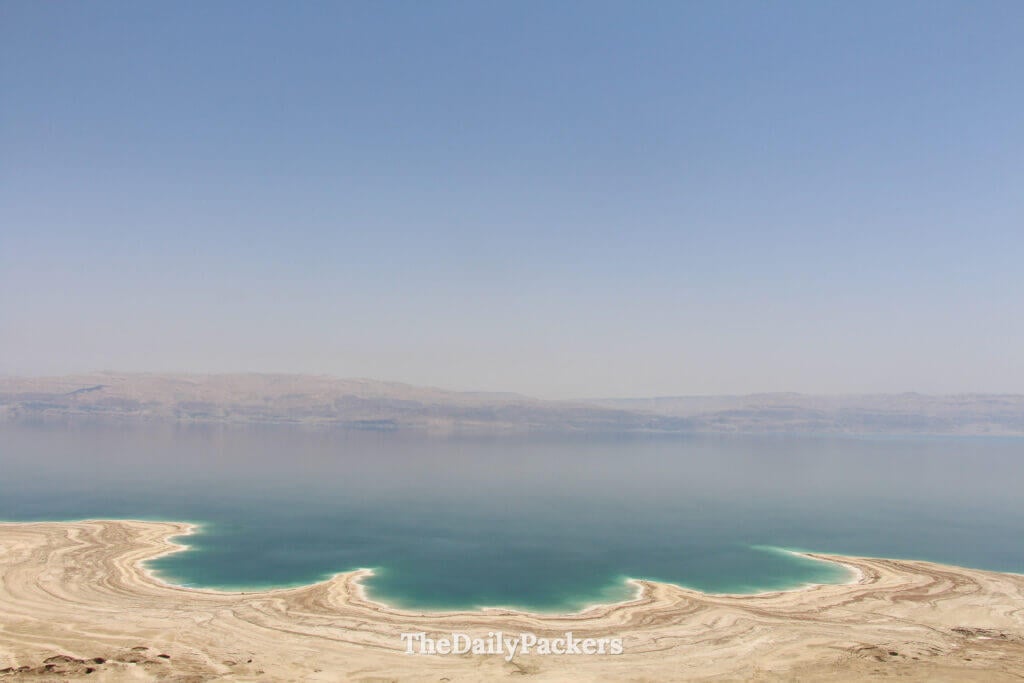 Panoramic viewpoint overlooking the Dead Sea with turquoise water and layered salt formations along the shoreline