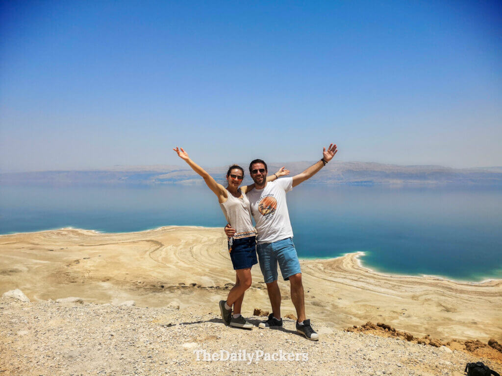 Couple posing at a Dead Sea viewpoint with arms raised, capturing the dramatic contrast between desert and water