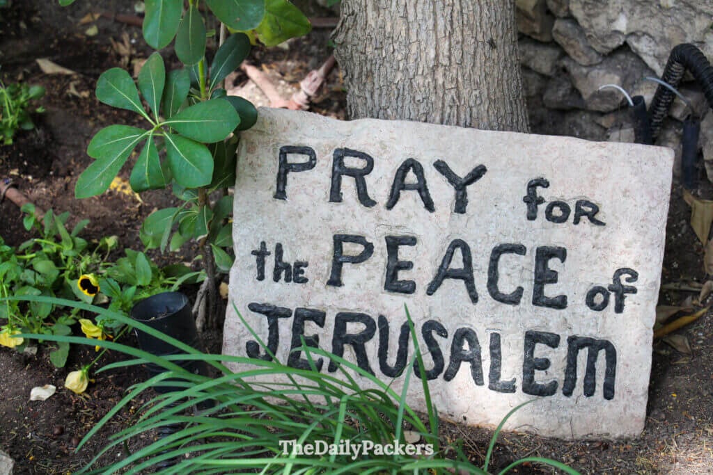 Stone sign reading Pray for the Peace of Jerusalem inside the Garden Tomb grounds, surrounded by plants and flowers
