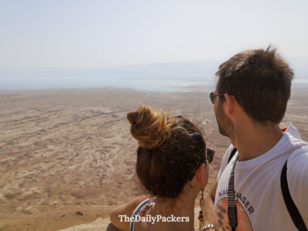 Couple standing at Masada viewpoint overlooking the desert plains and the Dead Sea region in the distance