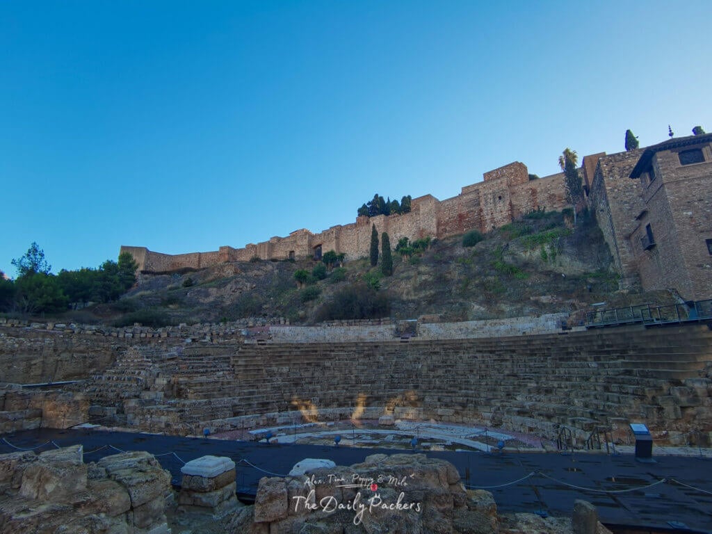 Vue grand angle du théâtre romain de Málaga avec la forteresse de l'Alcazaba qui le surplombe, montrant les terrasses de pierre antiques et les murs fortifiés sur le flanc de la colline.