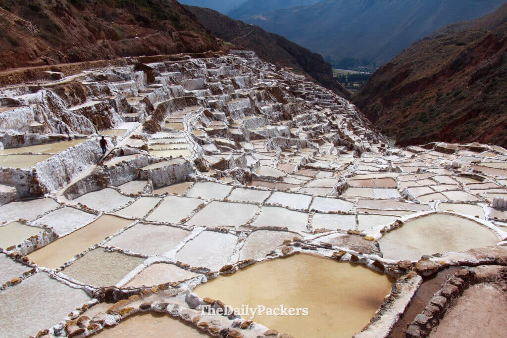 Vue panoramique des terrasses de sel de Maras dans la Vallée Sacrée du Pérou, avec des travailleurs marchant le long d’étroits sentiers entre les anciens bassins.