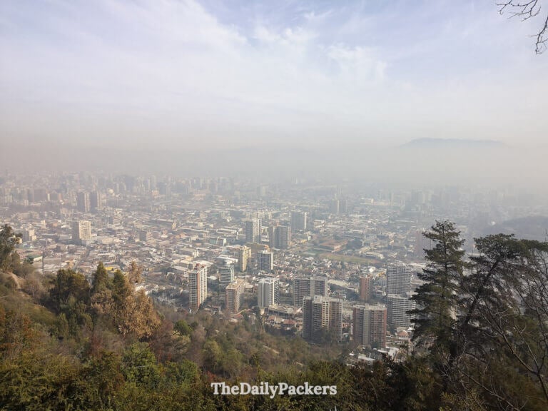 Wide view of Santiago de Chile from Cerro San Cristóbal, with residential towers and tree-covered hills stretching into the hazy distance.