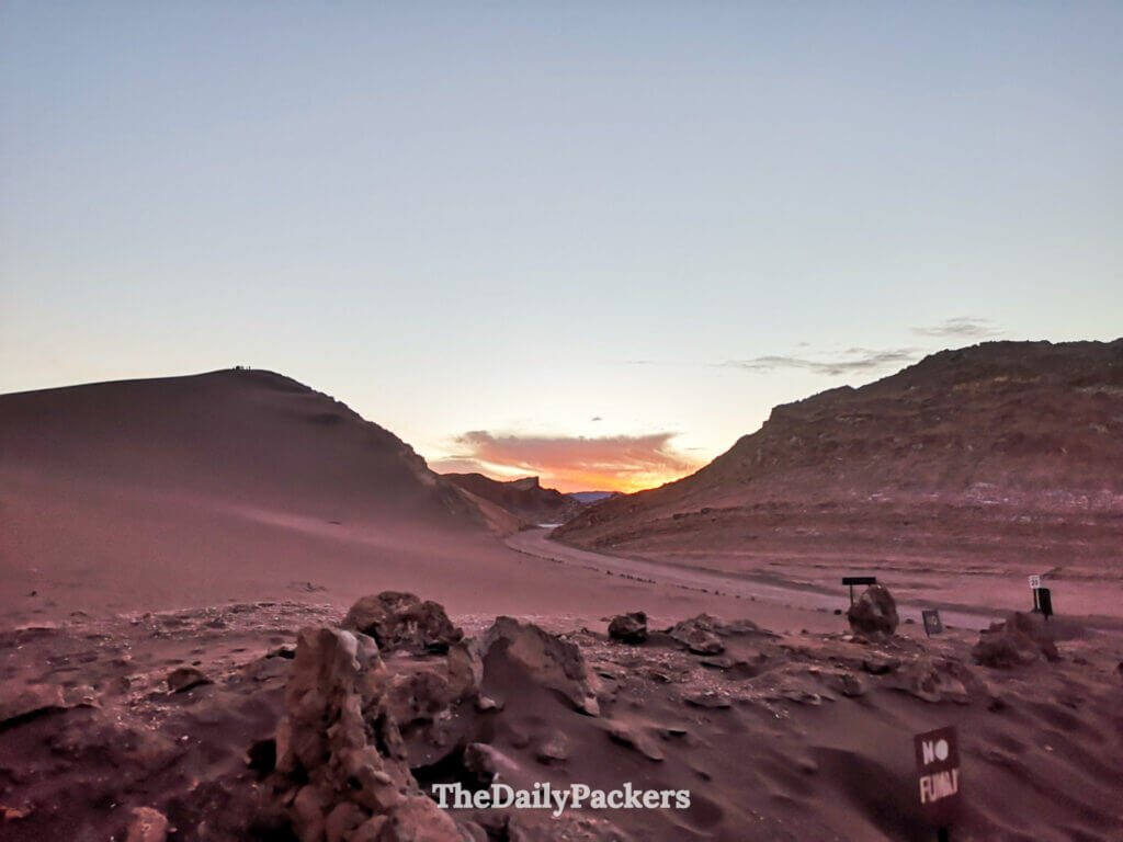 Evening light fading over a sand dune in Valle de la Luna, with silhouettes of visitors on the ridge and the sky turning pastel as sunset approaches.