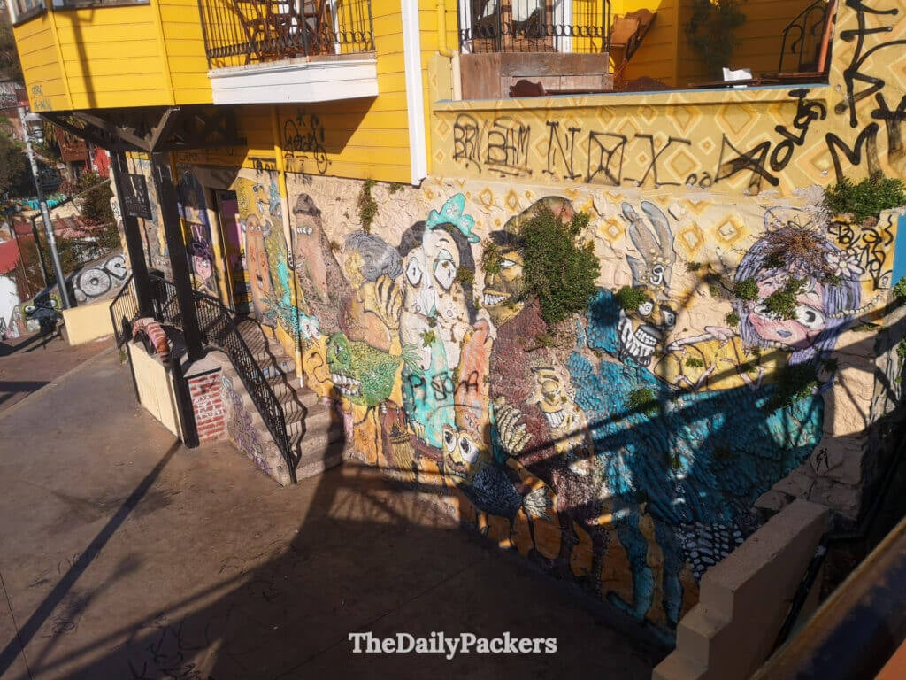 Fresque d'art de rue colorée sous une maison jaune sur le Paseo Dimalow, mettant en valeur la culture urbaine créative de Valparaíso dans le quartier de Cerro Alegre.