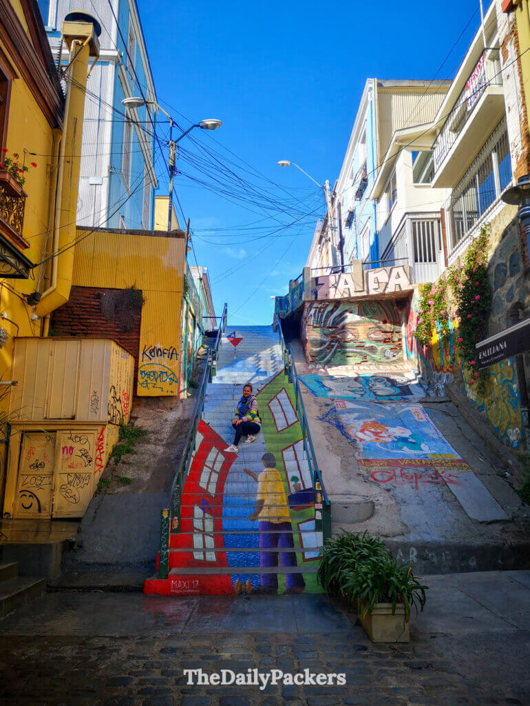 Escalier peint coloré dans Cerro Concepción, Valparaíso, avec des fresques vibrantes et un voyageur assis à mi-chemin entouré d'art de rue et de maisons à flanc de colline.