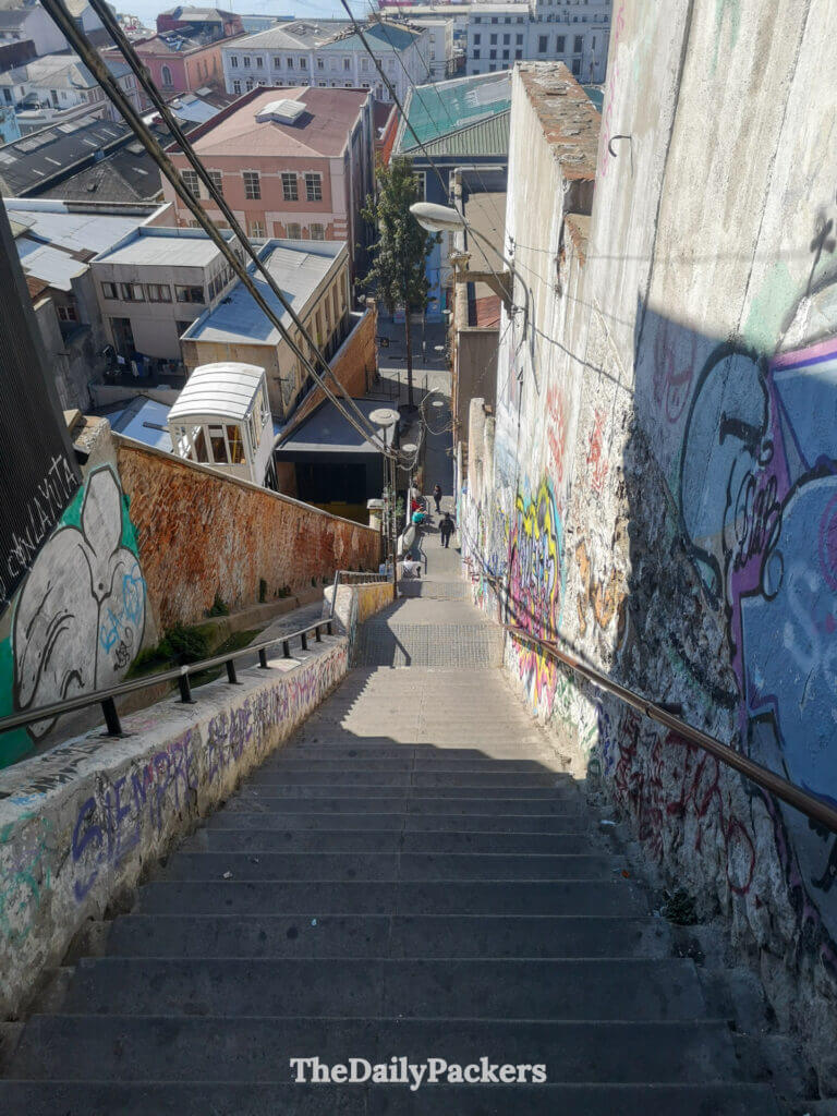 Escalier escarpé couvert de graffitis descendant du Cerro Alegre vers la ville basse, offrant une vue dégagée sur les toits et le port au loin.