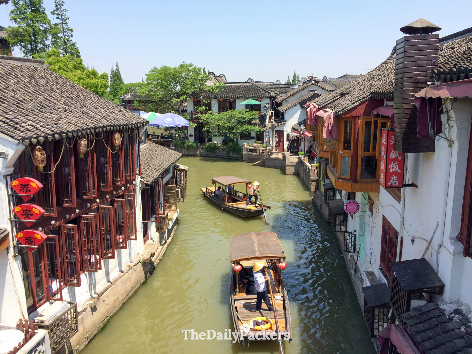 Canal traditionnel dans la ville d’eau de Zhujiajiao près de Shanghai, avec des bateaux en bois glissant devant des maisons historiques au bord de la rivière et des toits de tuiles vus depuis un pont de pierre