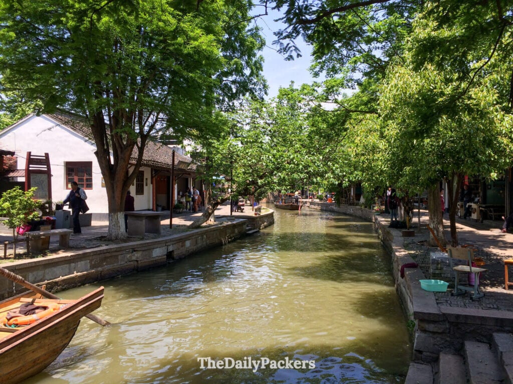 Canal ombragé à Zhujiajiao bordé d'arbres, de berges en pierre et de petits bateaux en bois créant une atmosphère paisible de ville d'eau