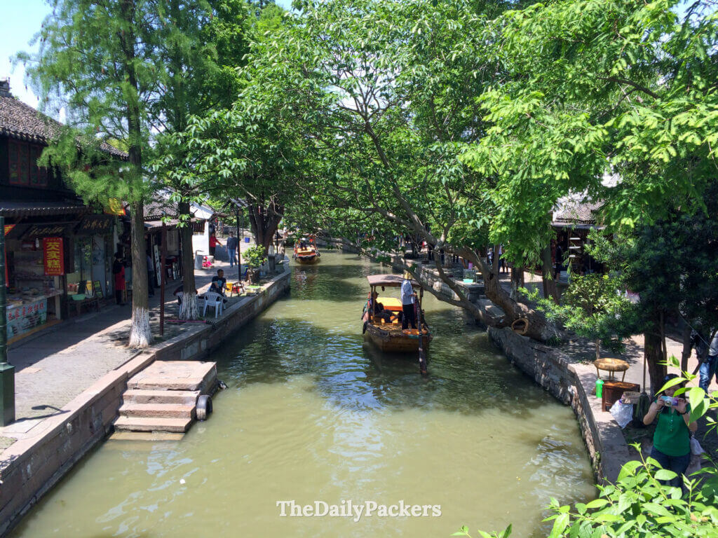 Scène de canal calme à Zhujiajiao avec des maisons traditionnelles, des arbres feuillus et de l'eau calme reflétant le charme de la ville ancienne