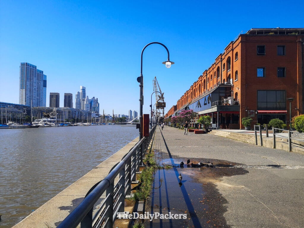 Walkway along Puerto Madero in Buenos Aires, showing red brick warehouses, river views, and the modern city skyline.