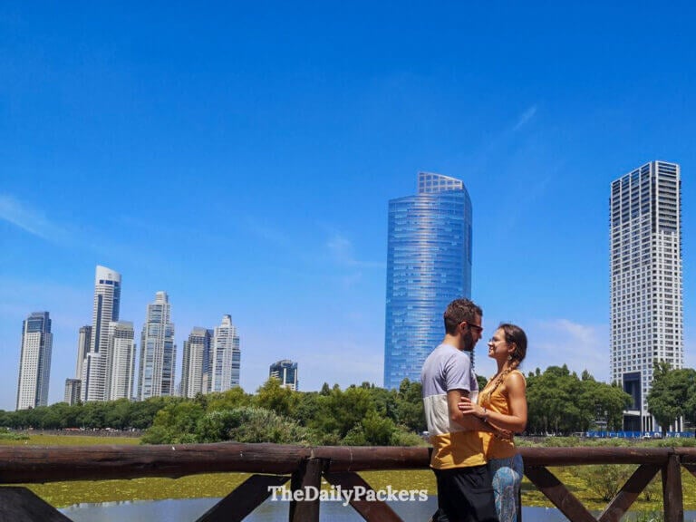 Couple standing at a wooden railing in Costanera Sur Ecological Reserve, Buenos Aires, looking toward the city skyline across the wetlands.