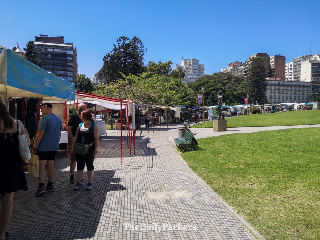 Plaza Francia flea market in Recoleta, Buenos Aires, with outdoor stalls, visitors, and city buildings in the background.