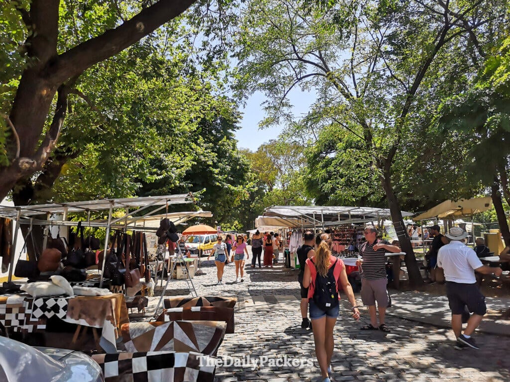 Marché en plein air sur la Plaza Francia à Recoleta, Buenos Aires, avec des stands d’artisans, des visiteurs qui circulent entre les étals et des arbres qui offrent de l’ombre.