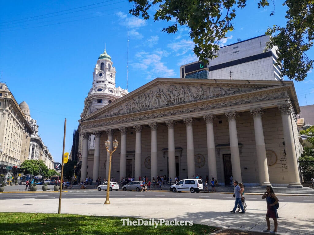 Exterior of Buenos Aires Metropolitan Cathedral on Plaza de Mayo, showcasing its neoclassical columns and busy city surroundings.