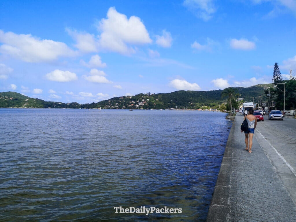 View over Lagoa da Conceição waterfront in Florianópolis, with calm lagoon waters, hills covered in houses, and a pedestrian walkway