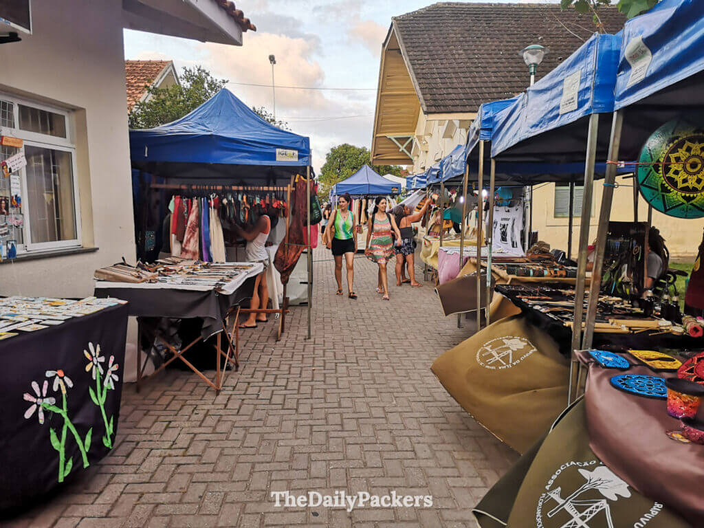 Street view of Lagoa da Conceição town in Florianópolis, showing colorful local market stalls, handmade crafts, and a relaxed evening atmosphere