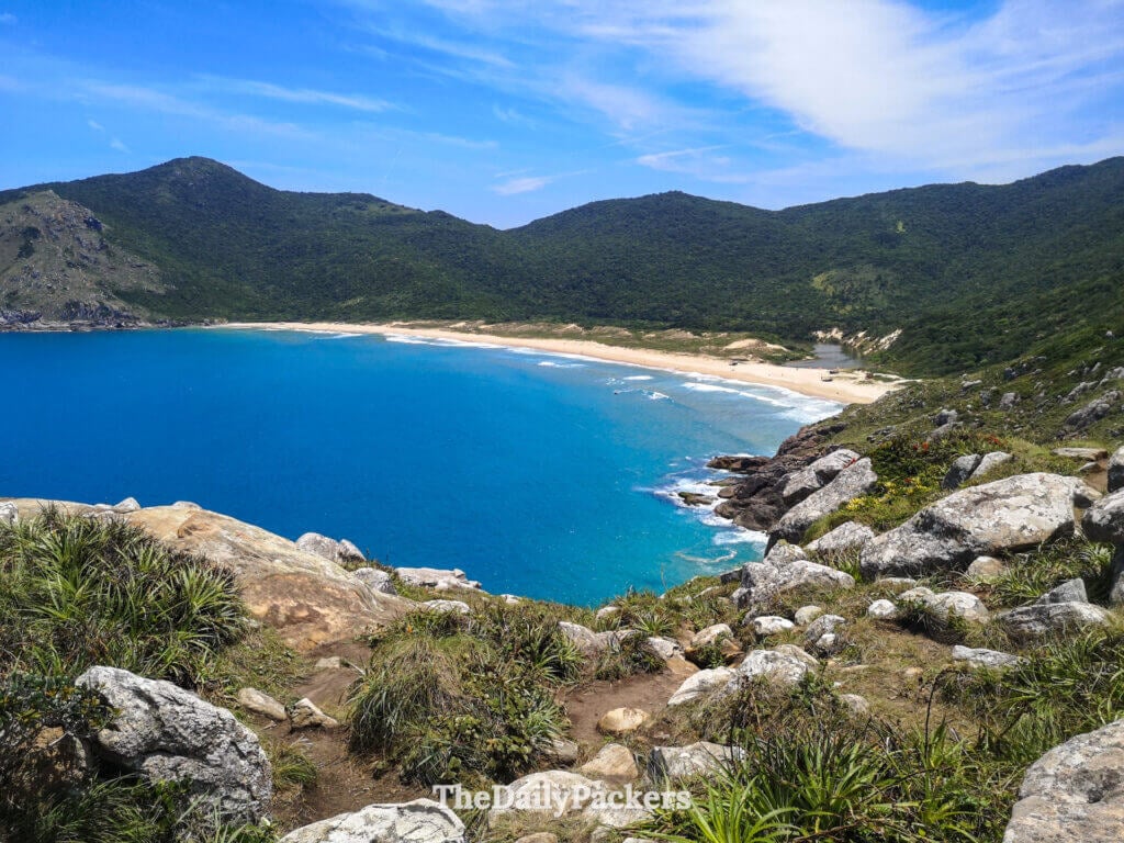 Vue panoramique de la plage de Lagoinha do Leste d’en haut, montrant de l’eau turquoise, un long rivage sablonneux et des collines verdoyantes intactes
