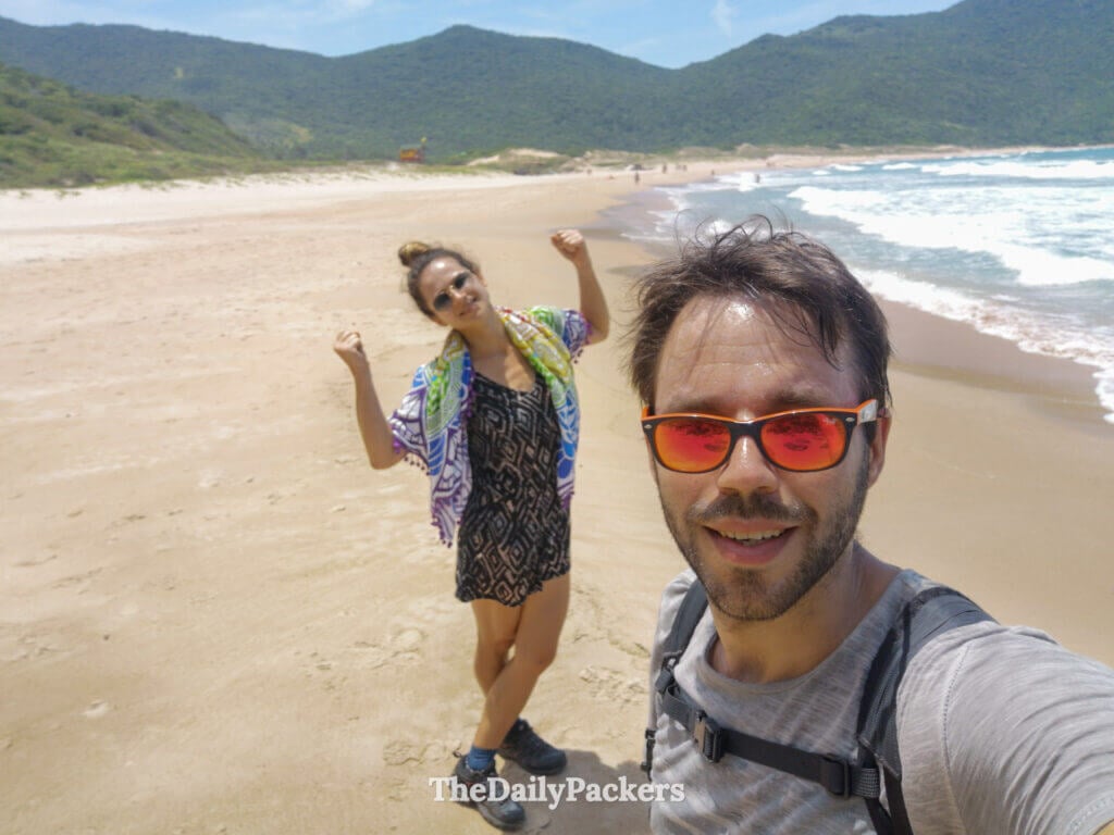 Selfie de couple à Lagoinha do Leste à Florianópolis, pris après la randonnée avec la plage sauvage et les collines boisées en arrière-plan