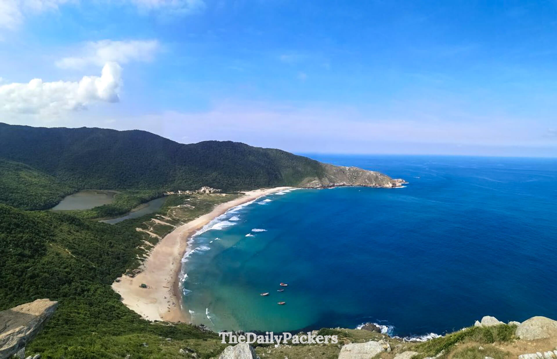 High-angle view over Lagoinha do Leste beach and lagoon in Florianópolis, with deep blue ocean, anchored fishing boats, and untouched coastline