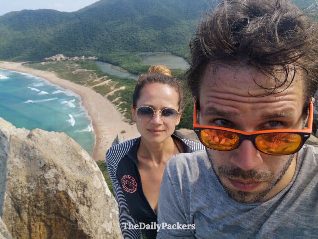 Selfie de couple pris au point de vue de Lagoinha do Leste, avec la plage, la lagune et les montagnes boisées visibles bien en contrebas