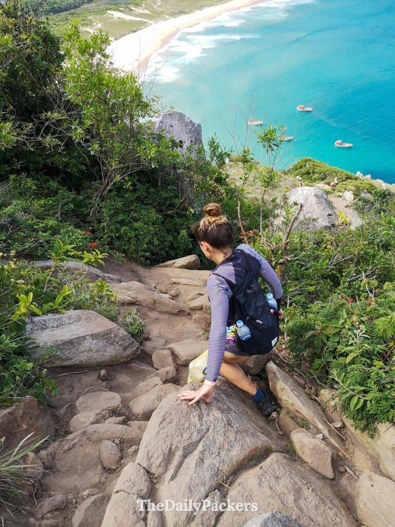 Descente rocheuse abrupte sur le sentier du point de vue de Lagoinha do Leste, avec des randonneurs descendant vers la plage et l’eau turquoise